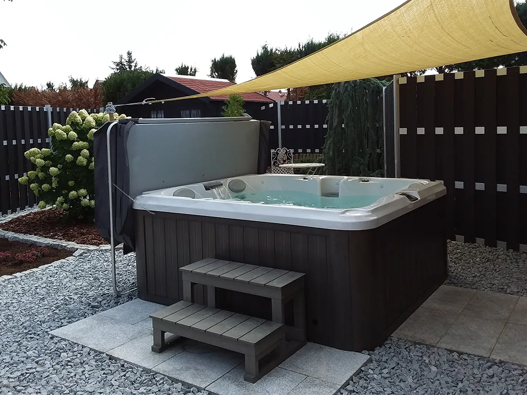 Kompakter Whirlpool Prado in einem gepflegten Gartenbereich mit Kiesboden und hellen Steinplatten.