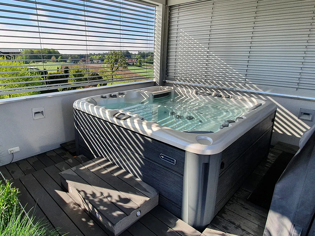 Whirlpool Cameo mit heller Verkleidung und offenem Deckel, auf grauem Terrassendeck mit Sonnenschirm.