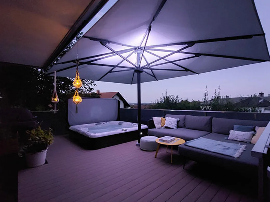 Whirlpool Cameo auf gemütlicher Terrasse bei Abendbeleuchtung, mit Lounge-Bereich unter großem Schirm.