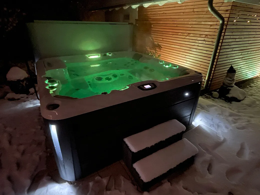 Whirlpool Cameo bei Nacht im Schnee, stimmungsvolle LED-Beleuchtung in Grün und Weiß.