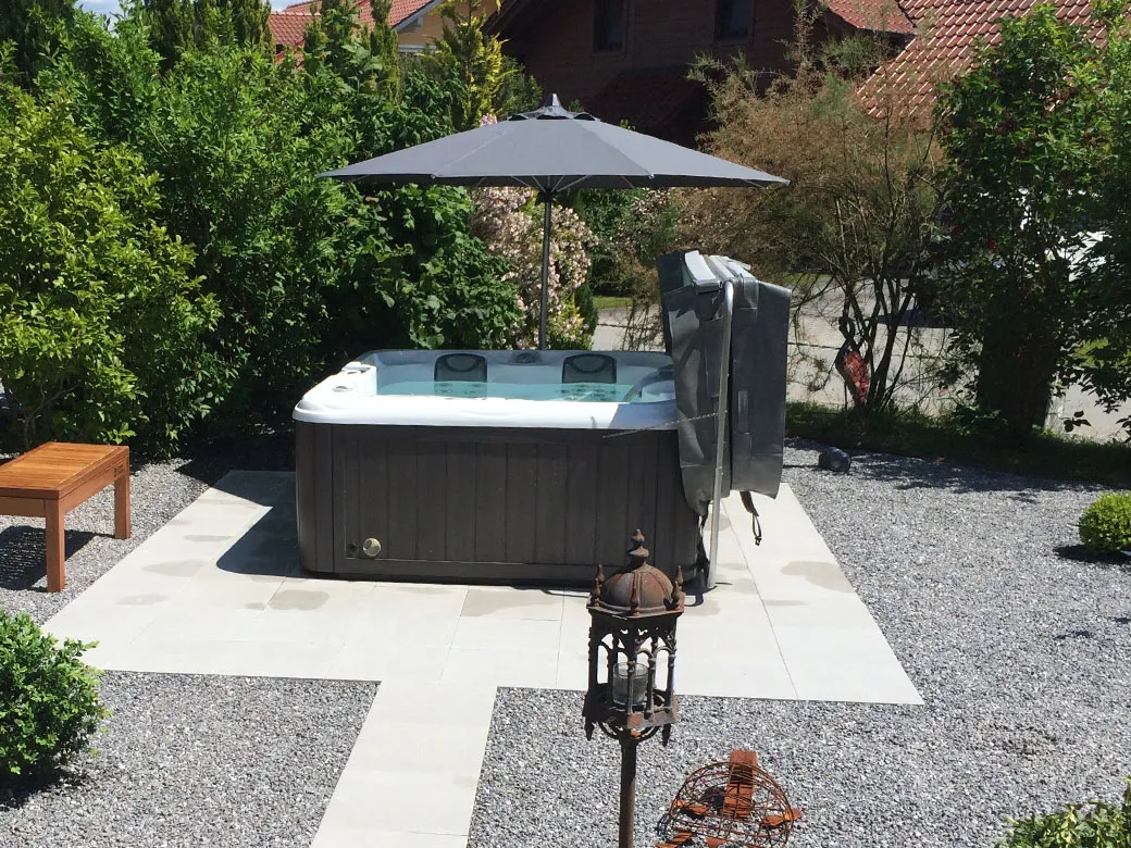 Whirlpool Capri im offenen Gartenbereich mit Sonnenschirm und umliegenden Ziersträuchern.