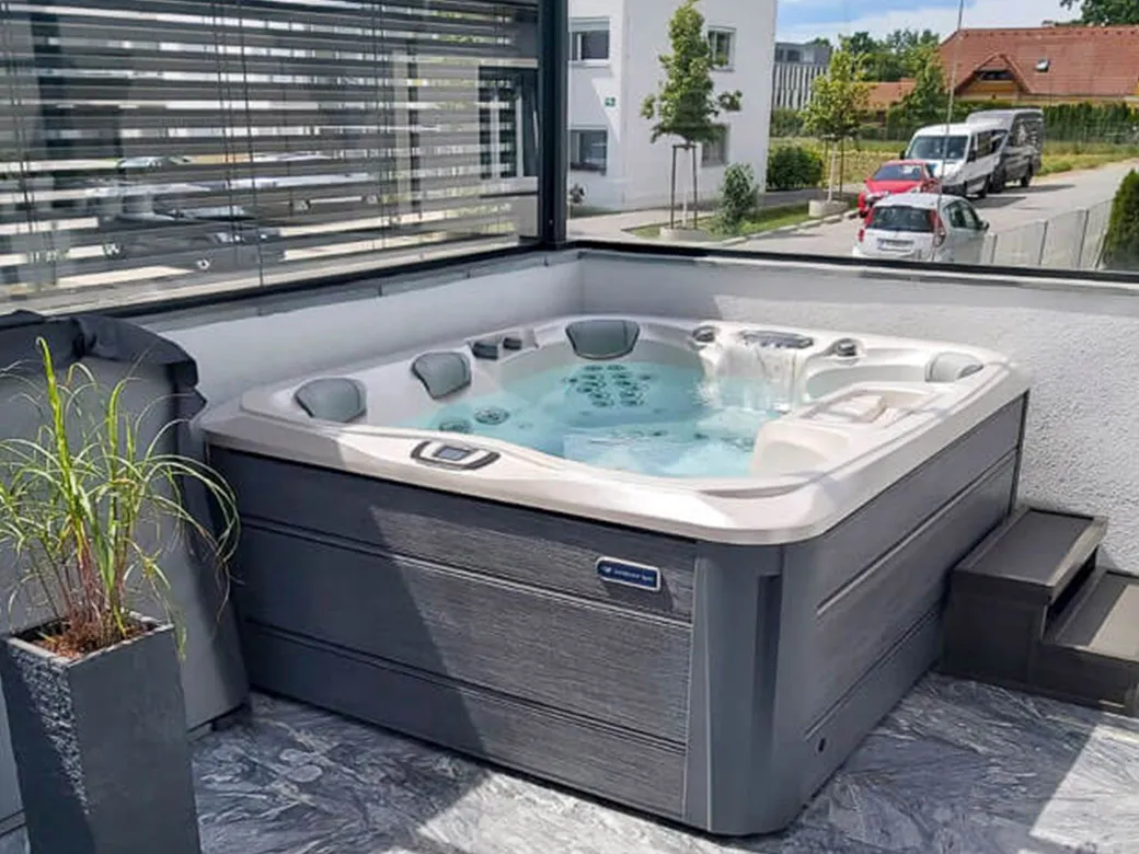 Whirlpool auf einer Steinfläche vor einer rustikalen Mauer – charmante Verbindung von Naturmaterialien und moderner Wellness.