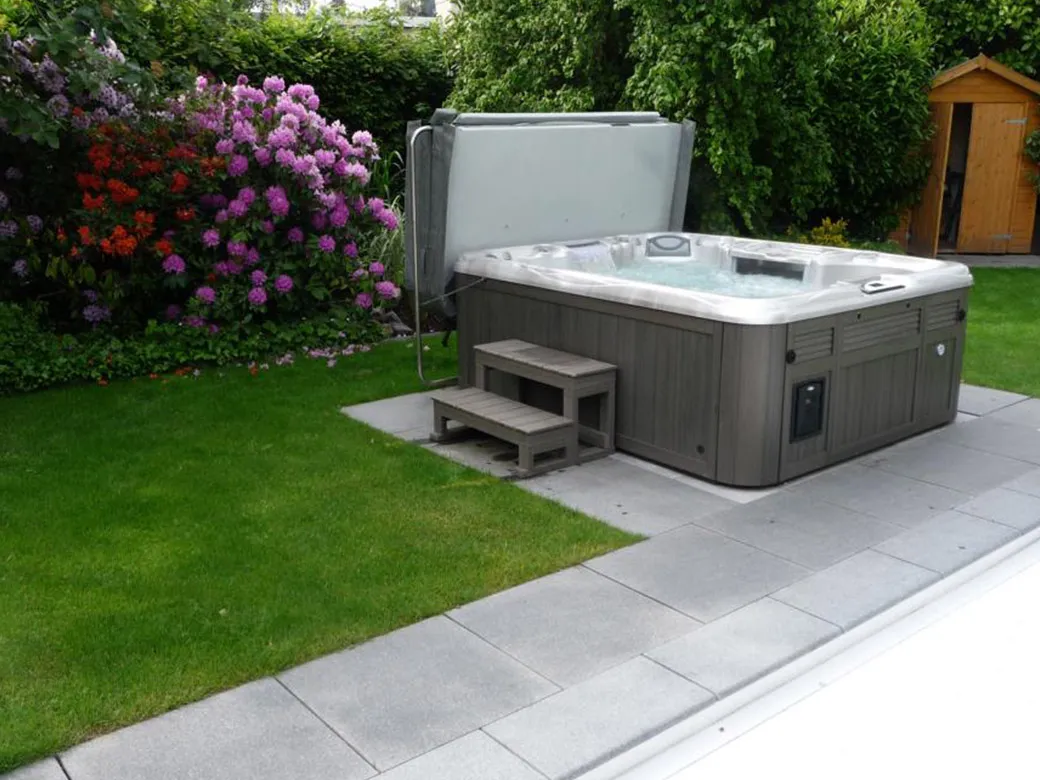 Whirlpool im gepflegten Garten – blühende Sträucher und Rasen schaffen eine idyllische Wellnessatmosphäre.